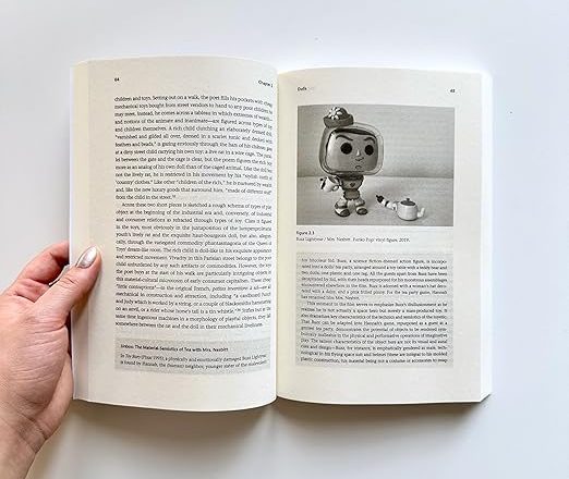 My book Toy Theory, held open at a page featuring an image of a Pop doll version of Buzz Lightyear as 'Mrs Nesbit' in Toy Story.